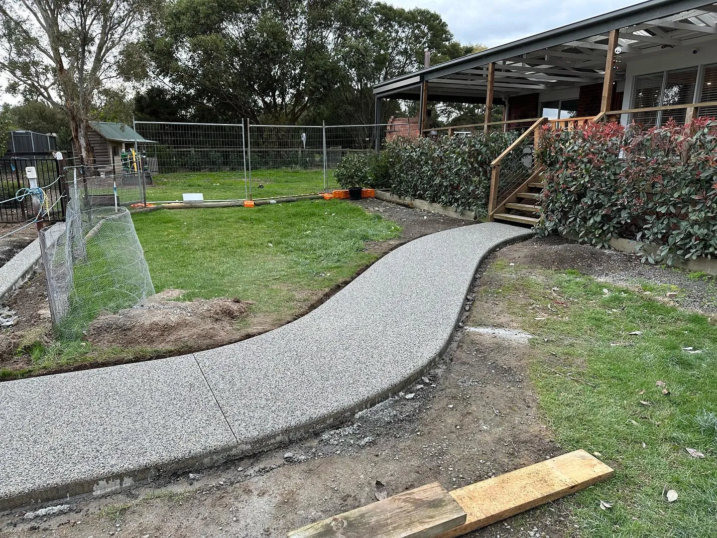 Curved exposed-aggregate path sweeping across the lawn toward the timber-deck verandah of a weatherboard home