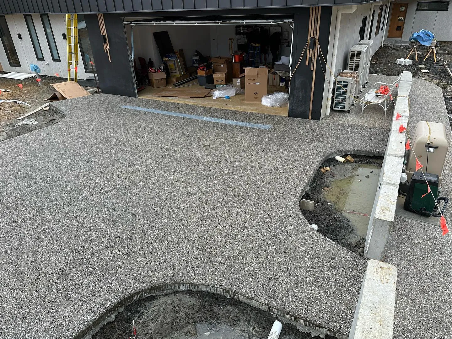 Wraparound exposed aggregate apron with pool cut-outs at a modern charcoal-clad architectural new build