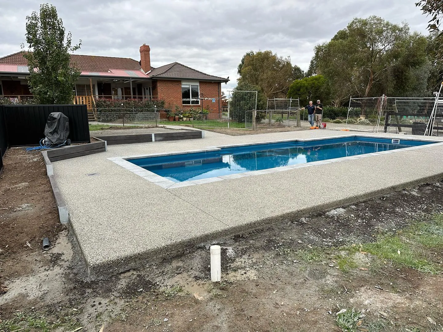 Wide exposed aggregate pool surround with a blue pool and a period weatherboard home behind