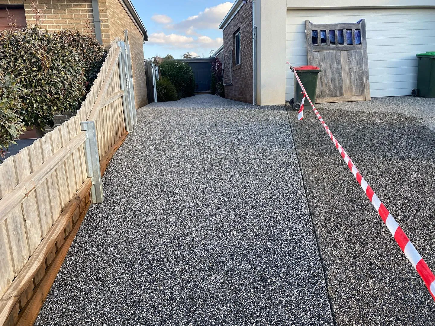 Finished dark exposed aggregate side driveway sealed off behind a double gate