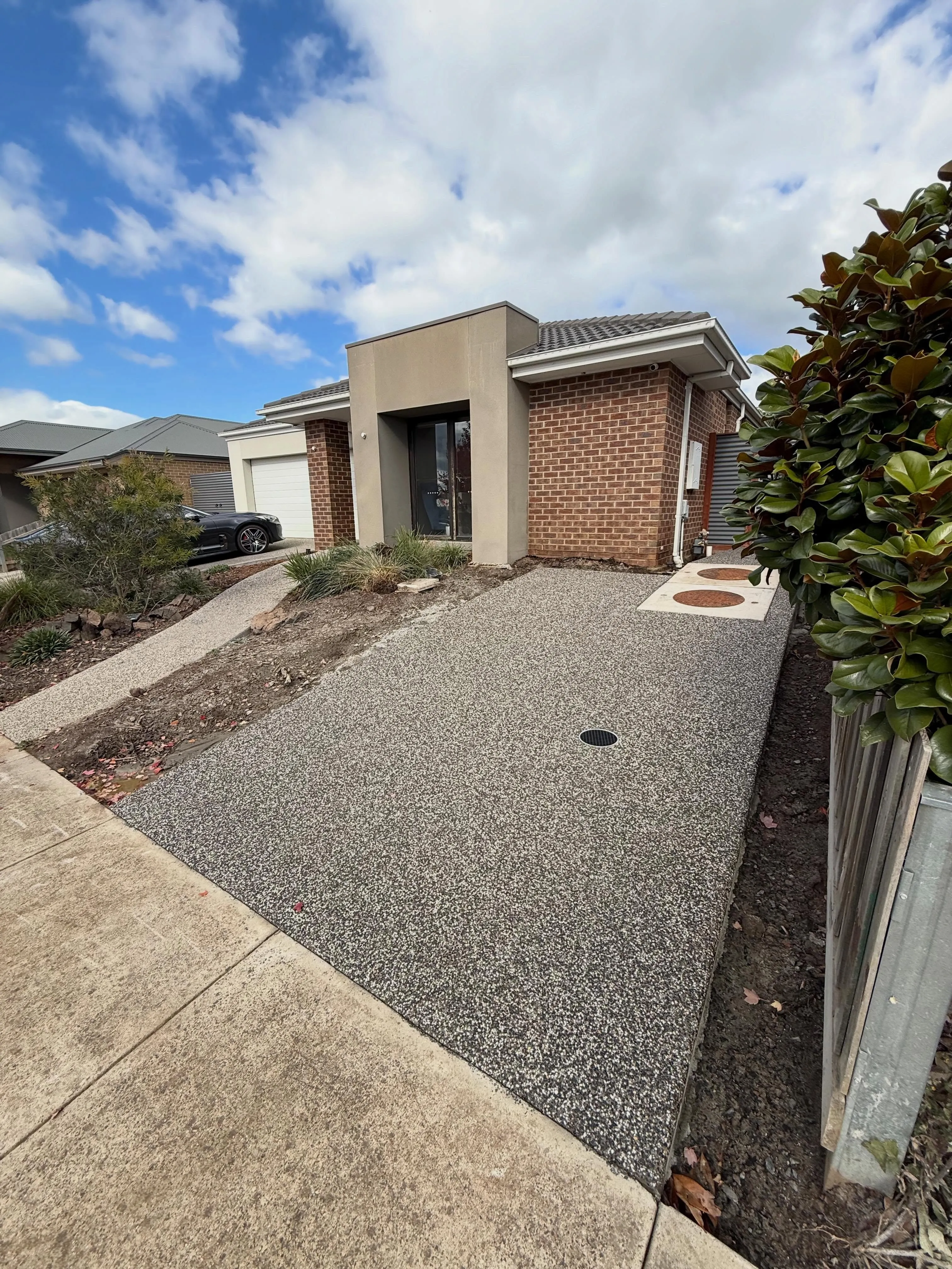 Exposed aggregate driveway at a modern stucco home under a big sky