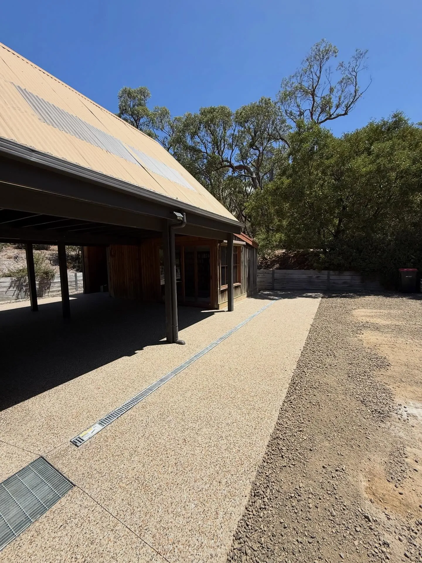 Wraparound exposed aggregate apron under the verandah of the rust-roofed rural home with drain-channel detail