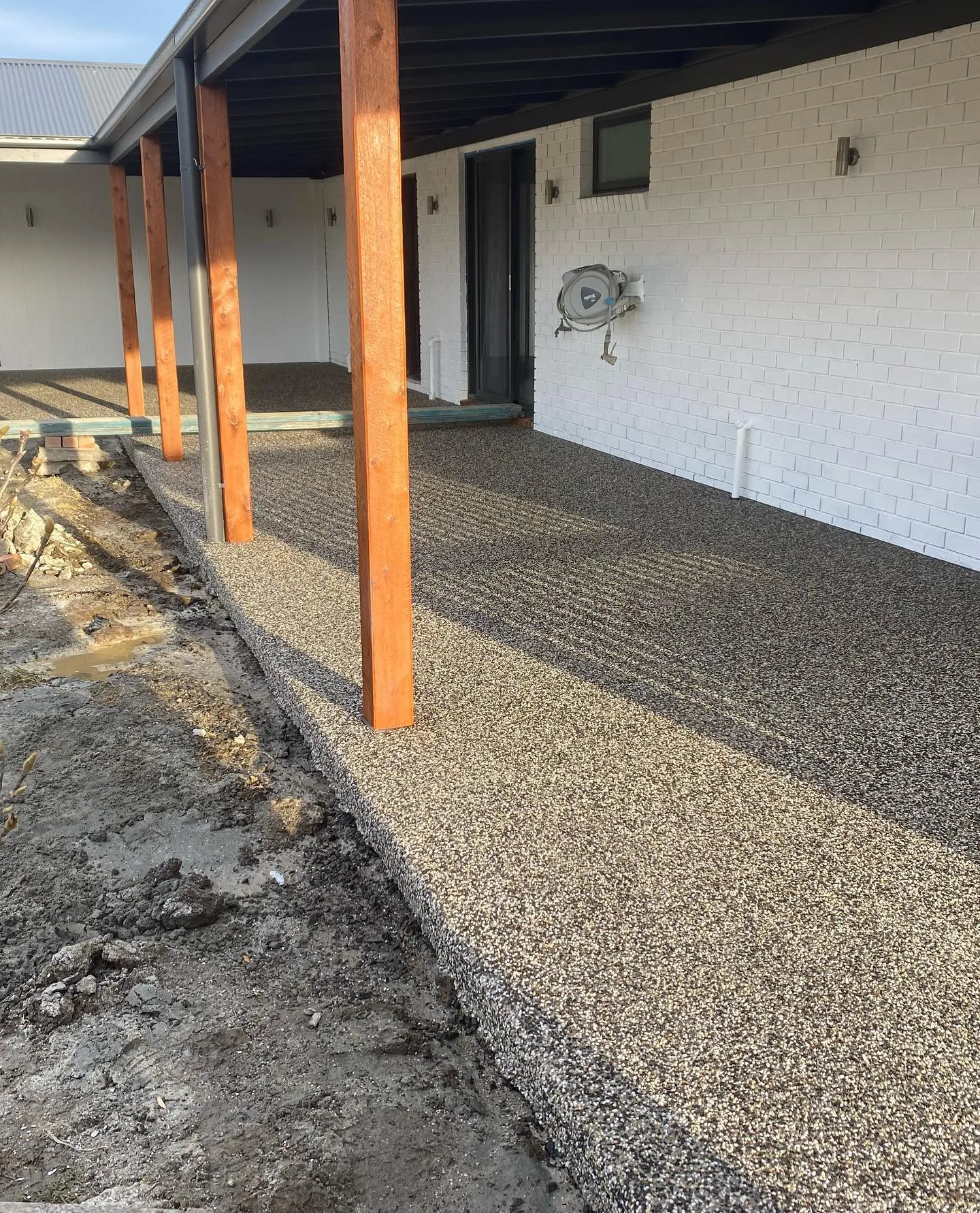 Exposed aggregate verandah and path wrapping a white brick home with timber porch posts
