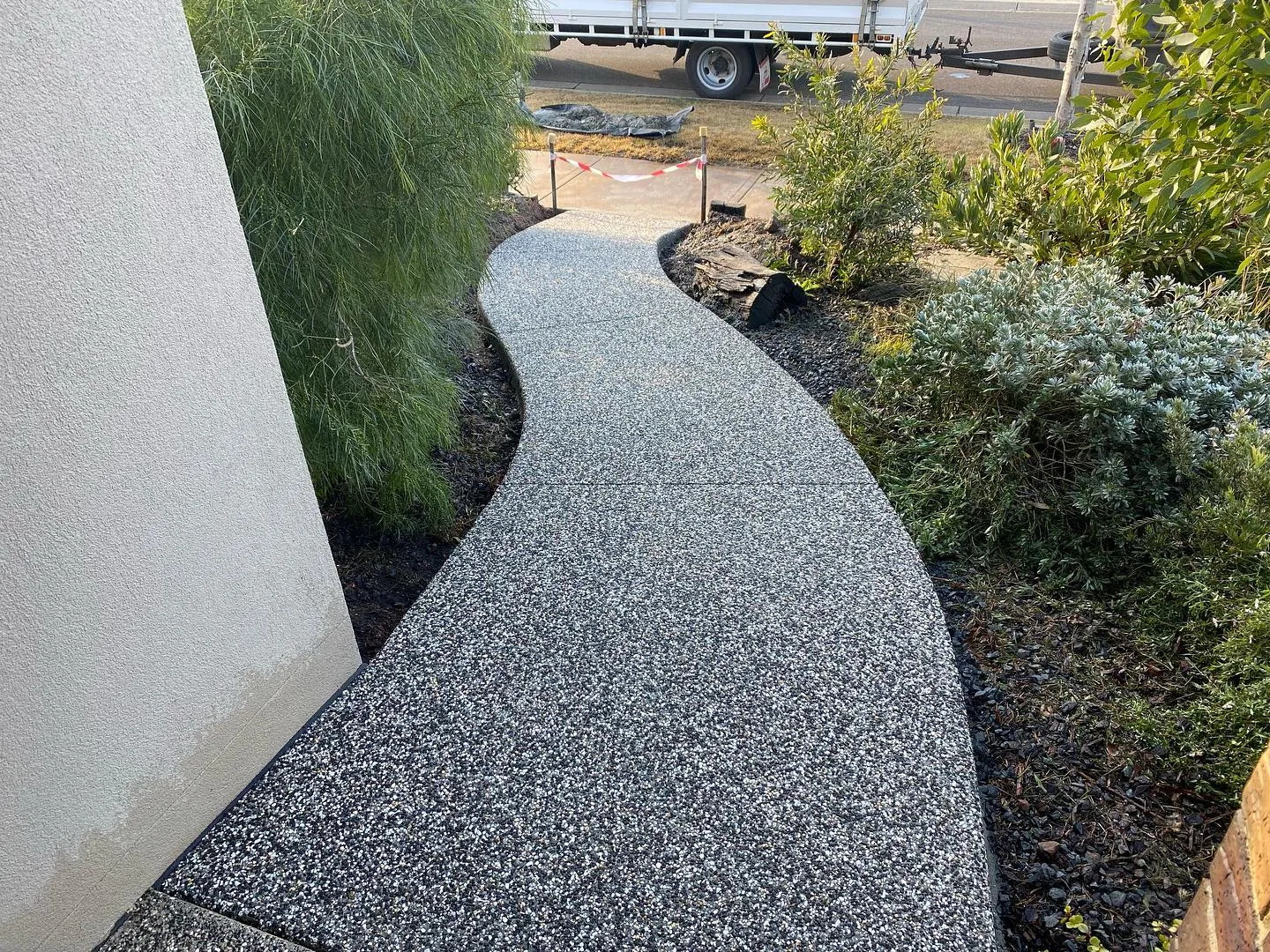 Curving exposed aggregate path winding past garden landscaping in late afternoon sun