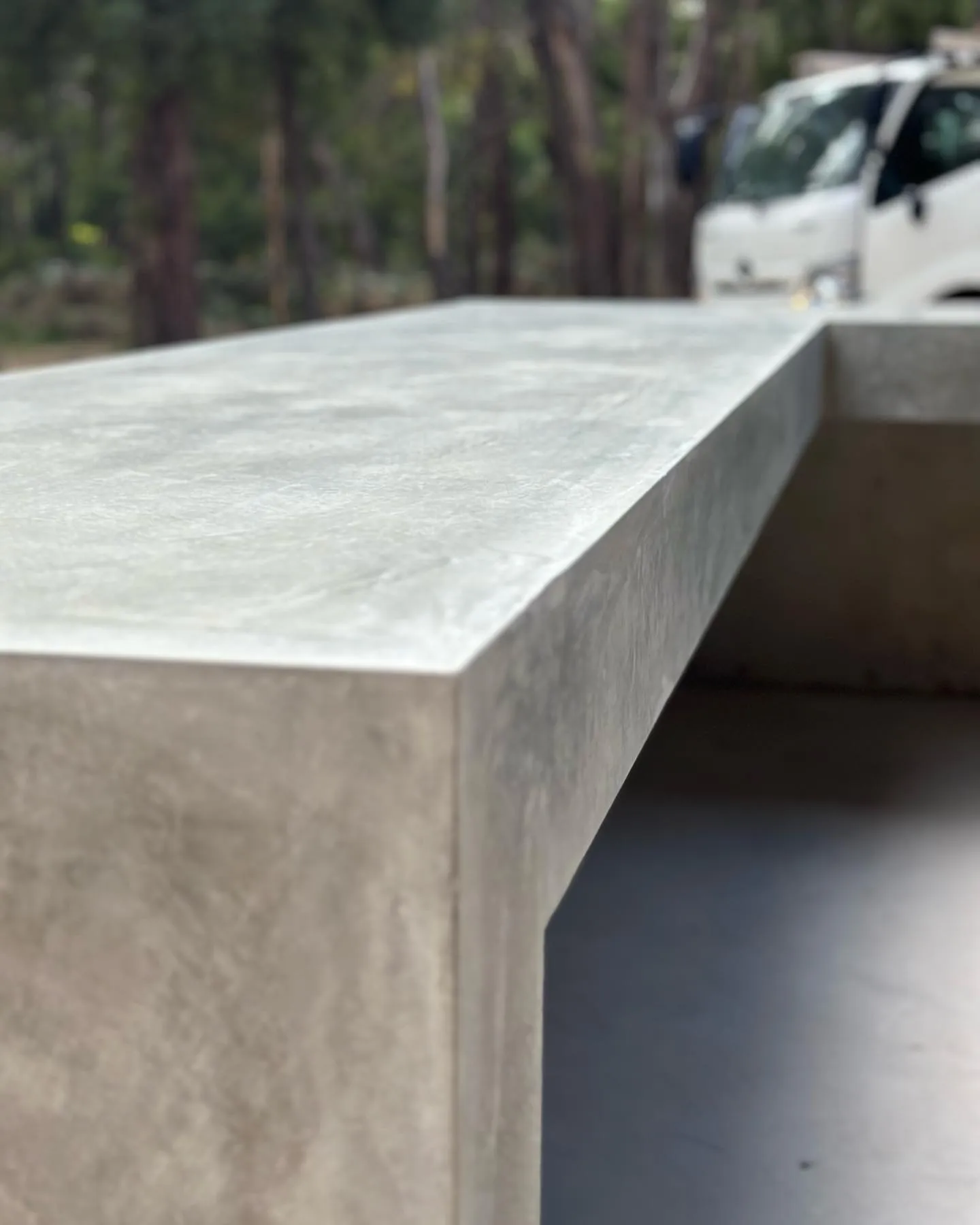 Macro close-up of the trowelled edge of the cast concrete bench, BMT truck softly out of focus behind