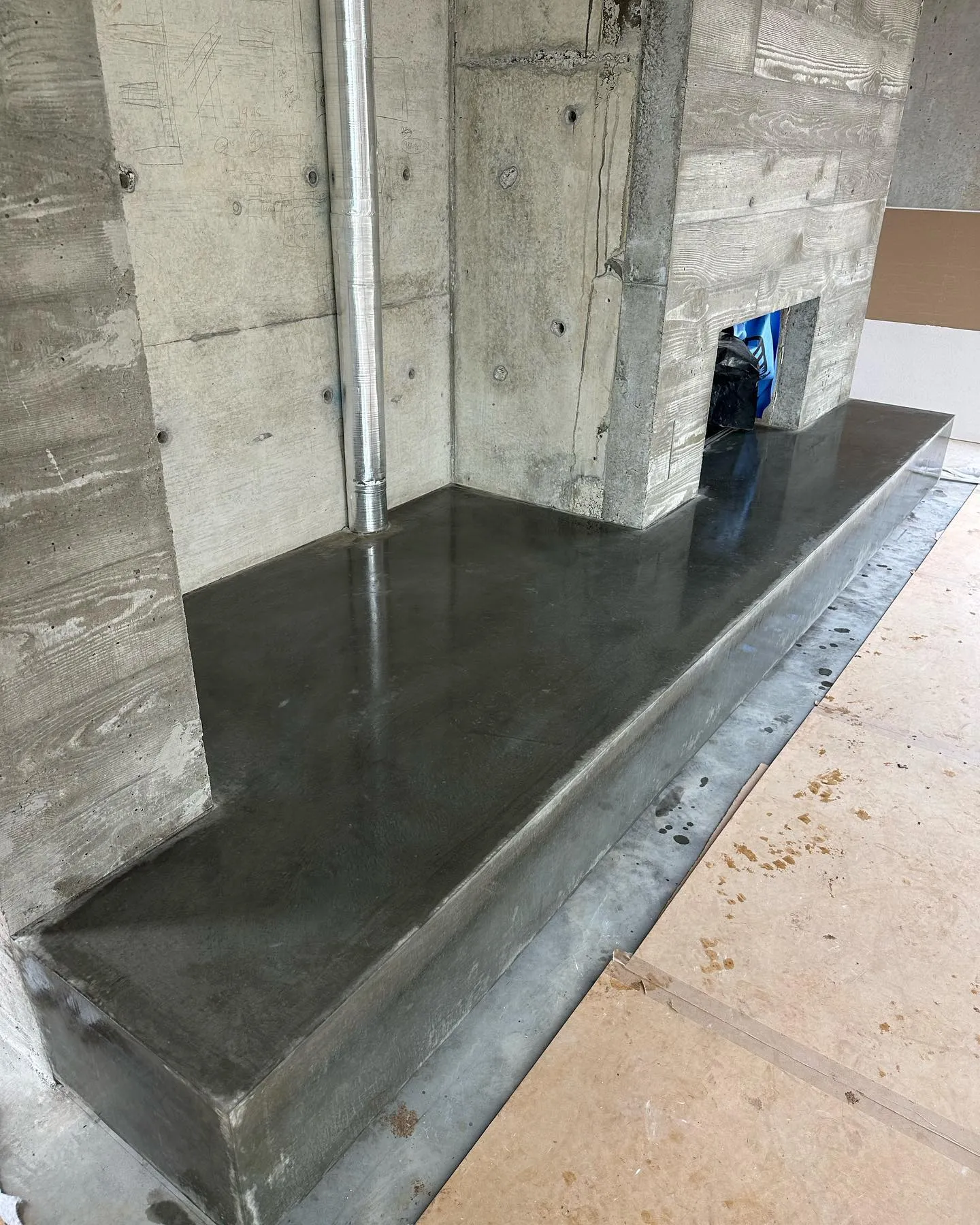 Charcoal off-form concrete fireplace hearth seated inside board-formed concrete walls, raw architectural finish