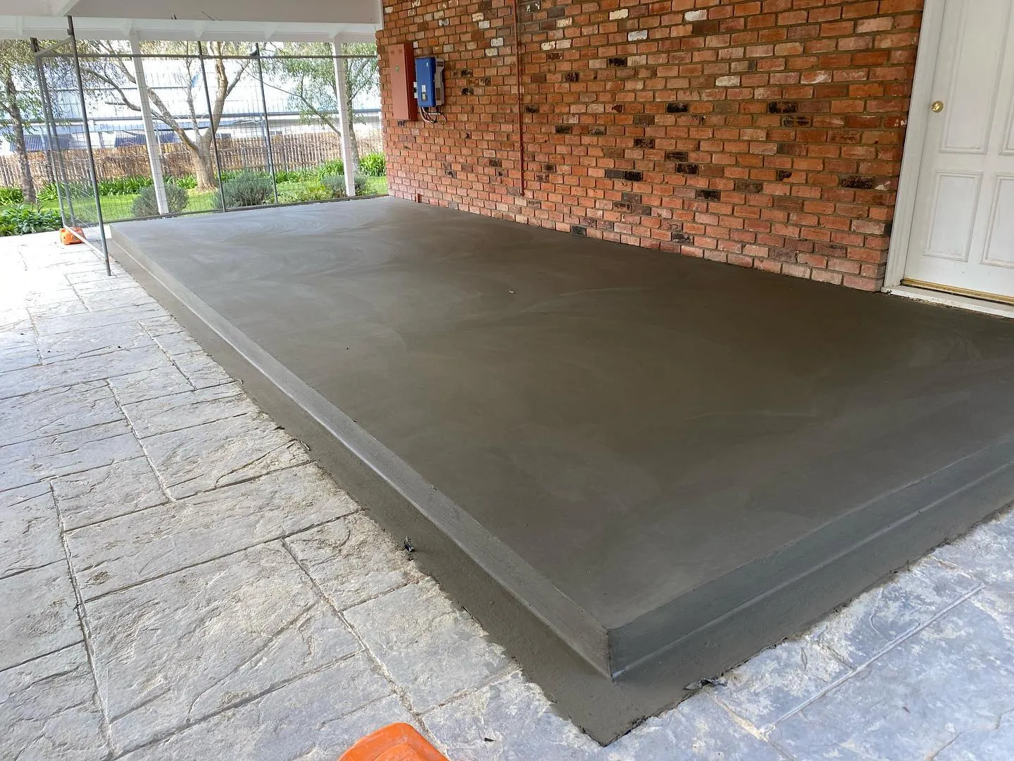 Charcoal-trowelled raised slab inset into bluestone crazy-paving against a brick wall