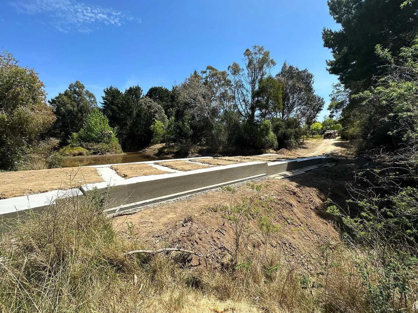 Long bridge formwork over a rural dam with rebar laid ready for the concrete pour, still water beside