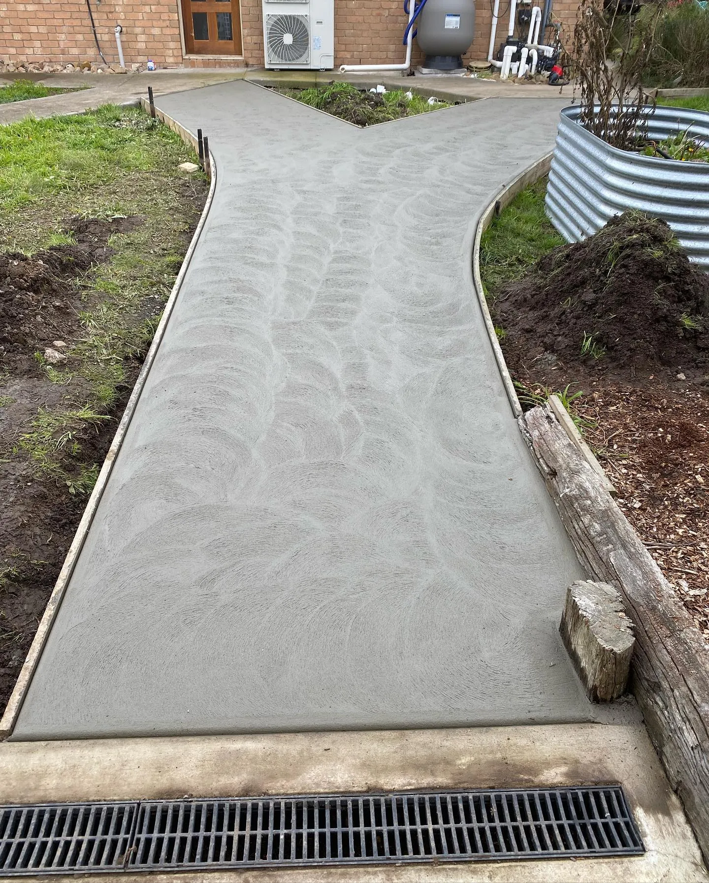 Decorative broom-finish forked concrete pathway with a curved edge against a corrugated tank