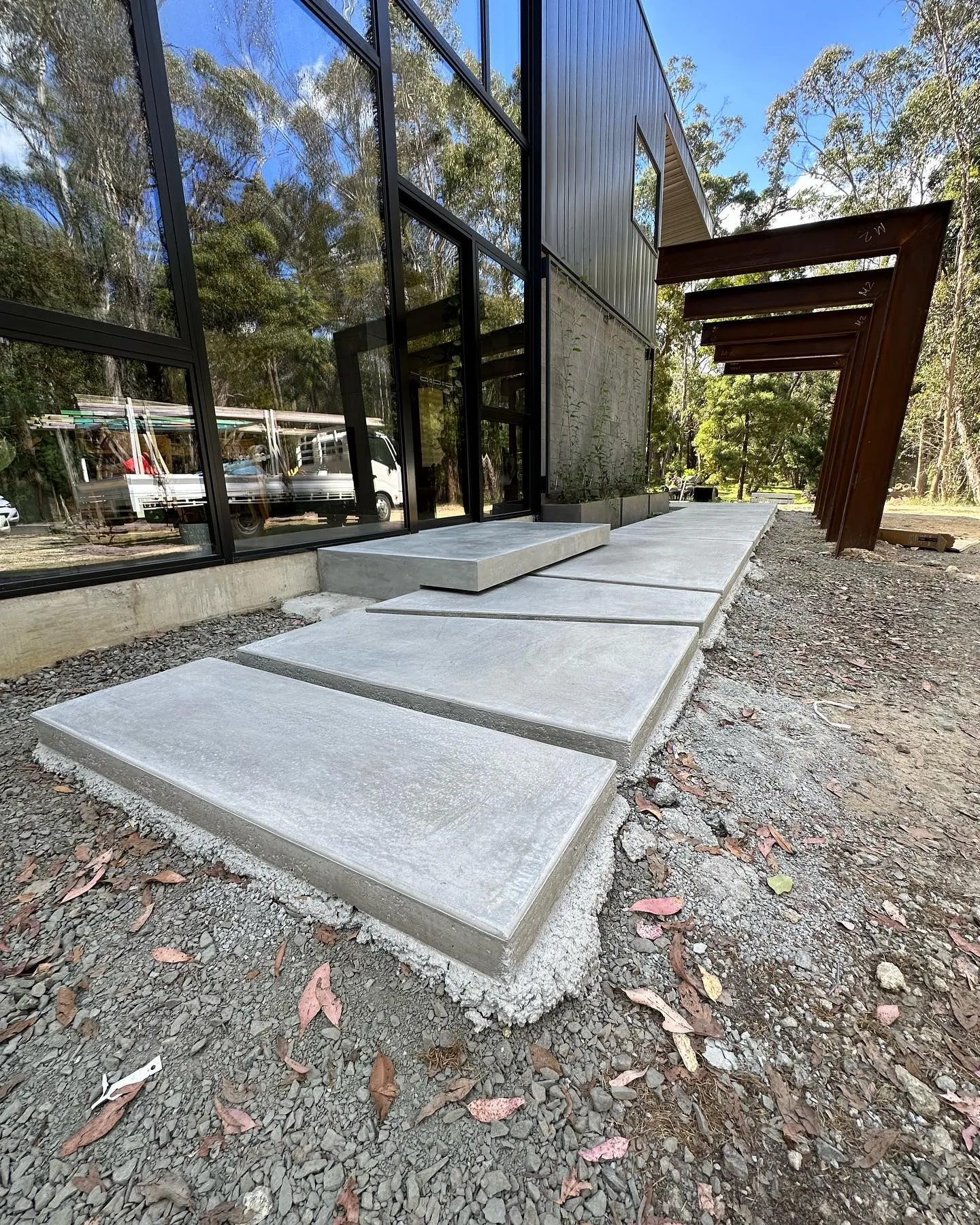 Staggered raised concrete slabs leading to a steel-and-glass architectural home entry