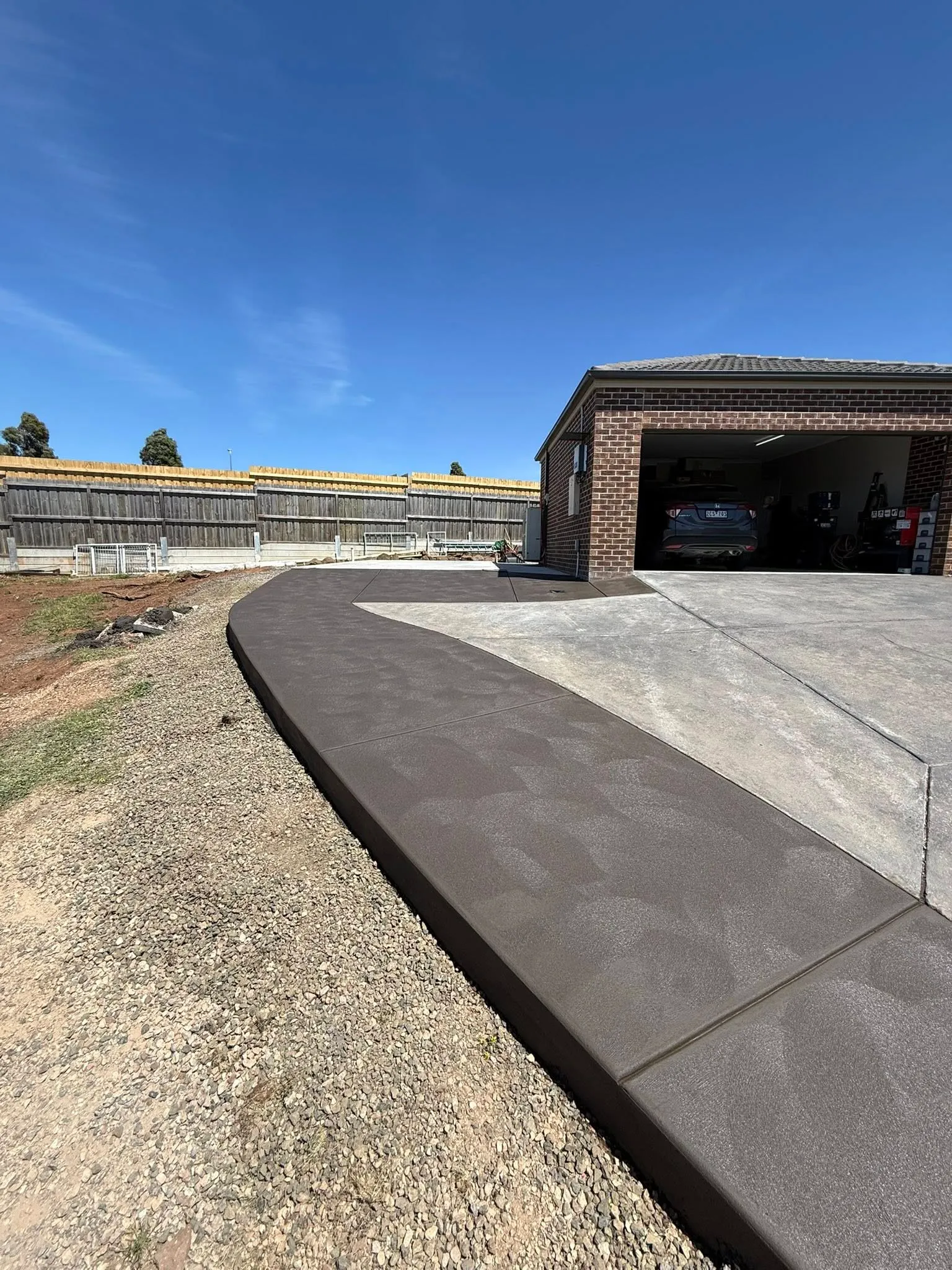 Two-tone driveway pairing a dark coloured strip with standard grey concrete at a brick home