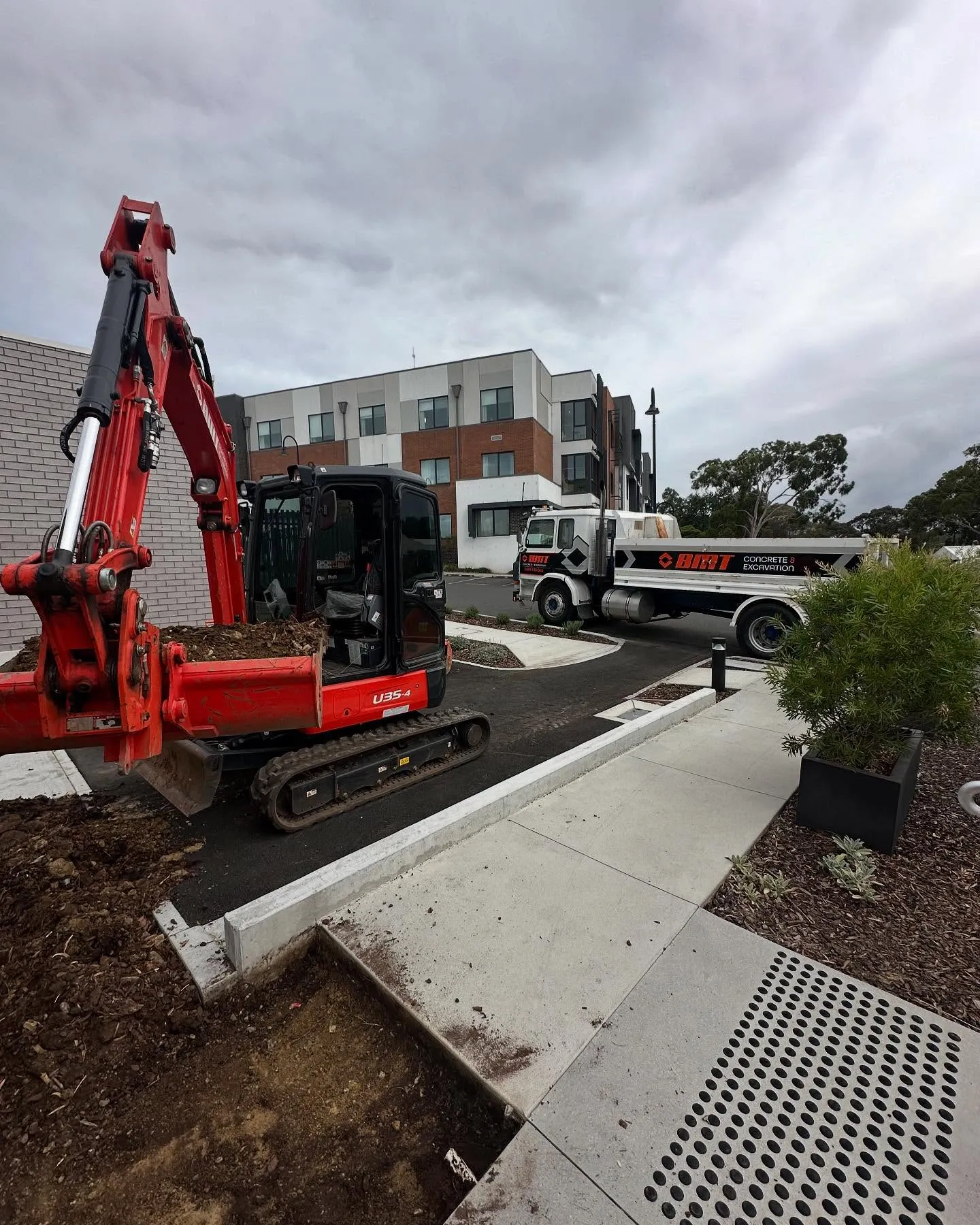 Kubota mini-excavator and BMT pump truck working a suburban infill site beside new townhouses, fresh path poured