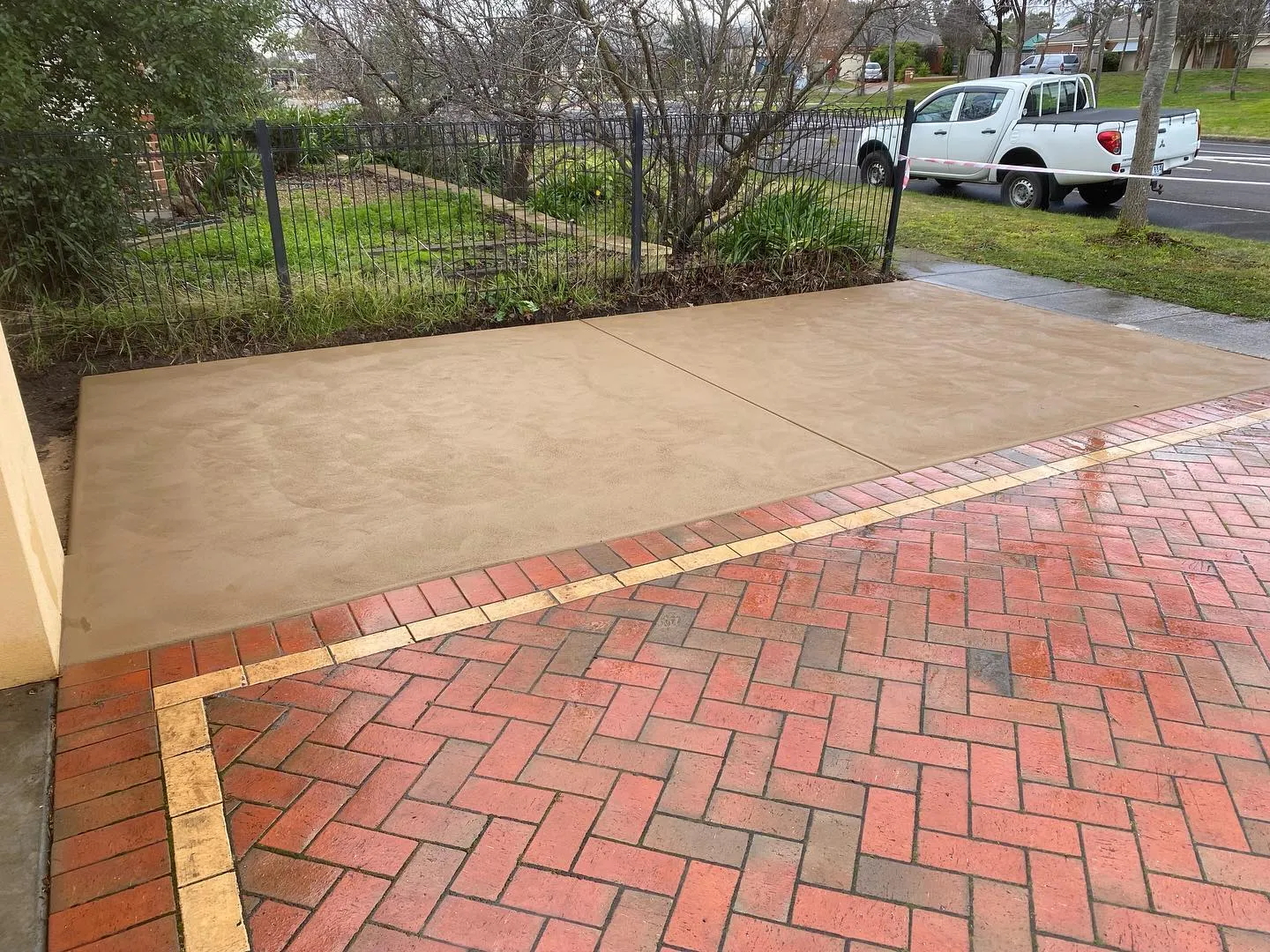 Coloured sandstone-tone concrete side entry pad meeting red herringbone brick paving