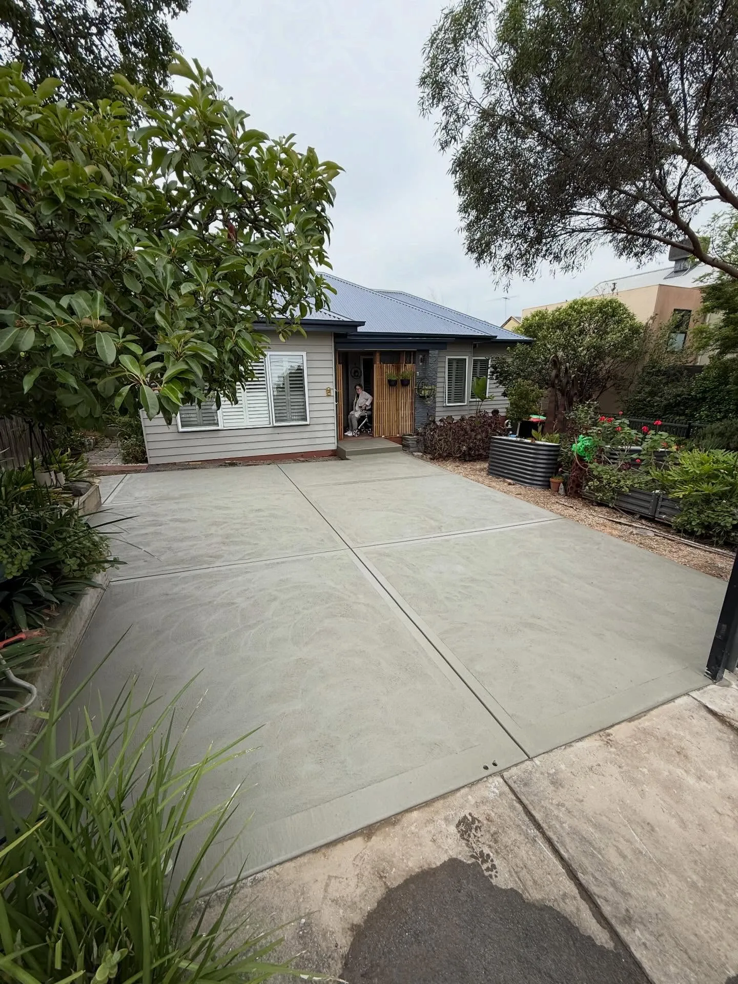 Wide plain-broom-finish concrete driveway with control joints leading to a blue-trim weatherboard cottage and tidy garden borders