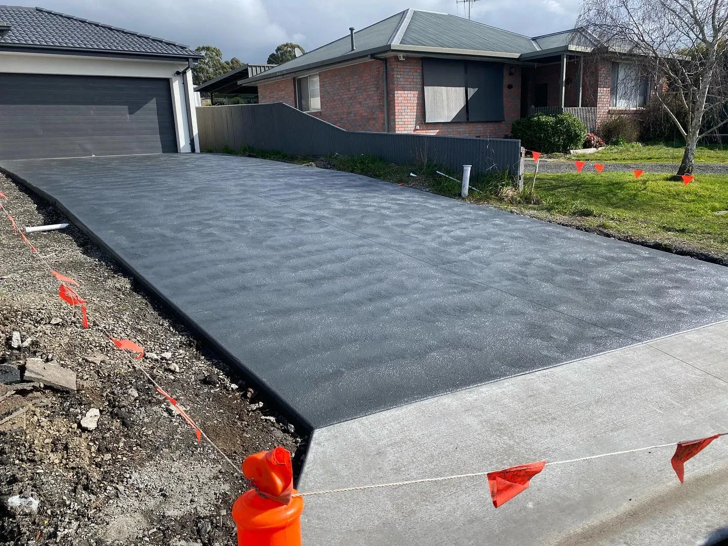 Finished charcoal coloured concrete driveway with sharp lines at a suburban home