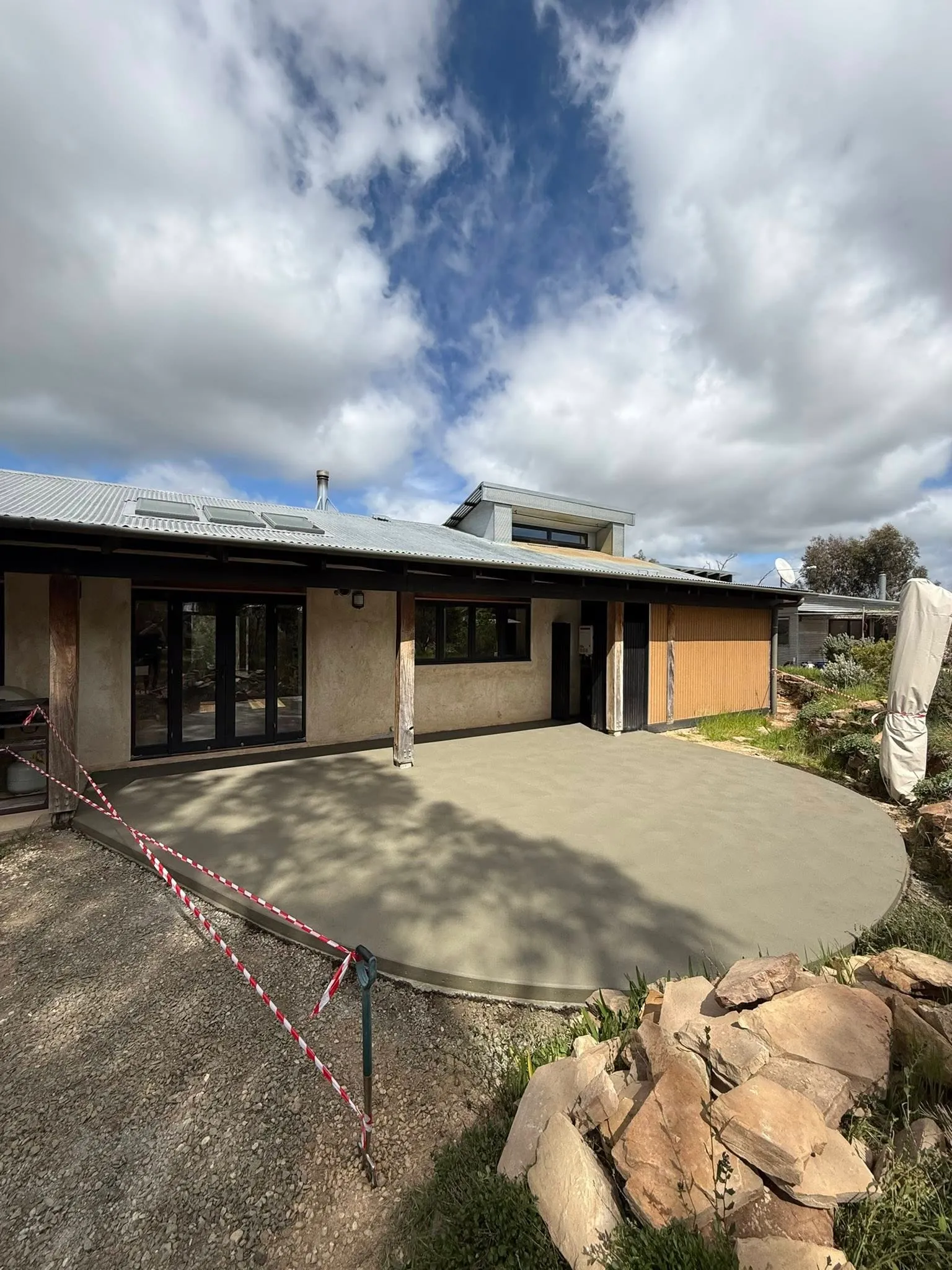 Curved freshly trowelled patio area at a mud-rendered home with stone landscaping