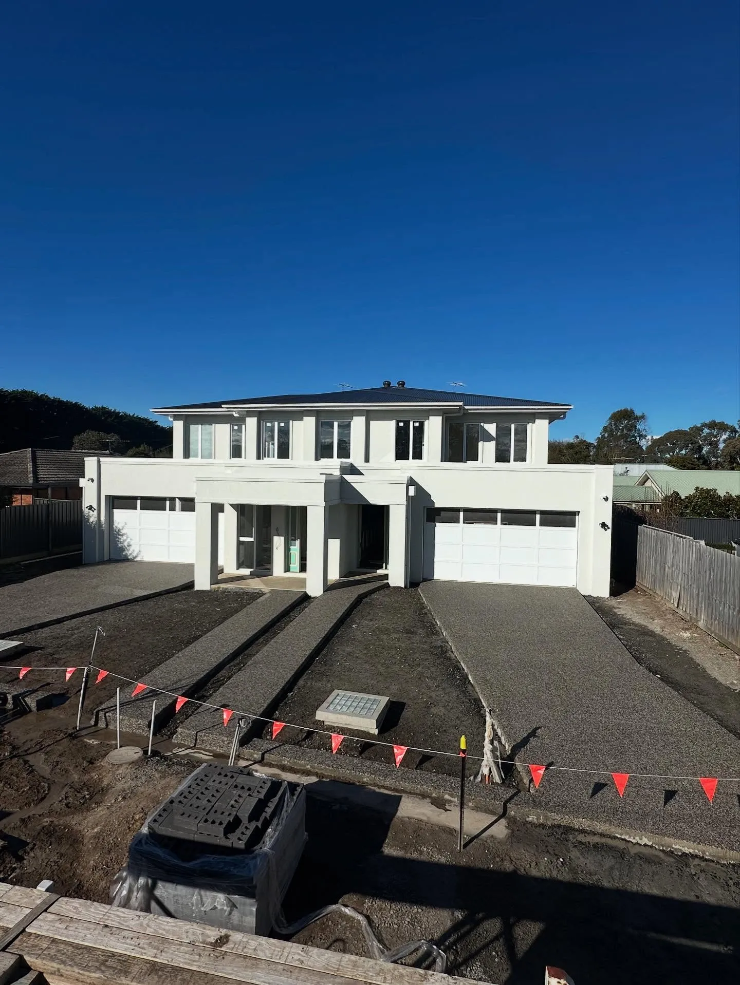 Twin exposed aggregate driveways at a large white two-storey home