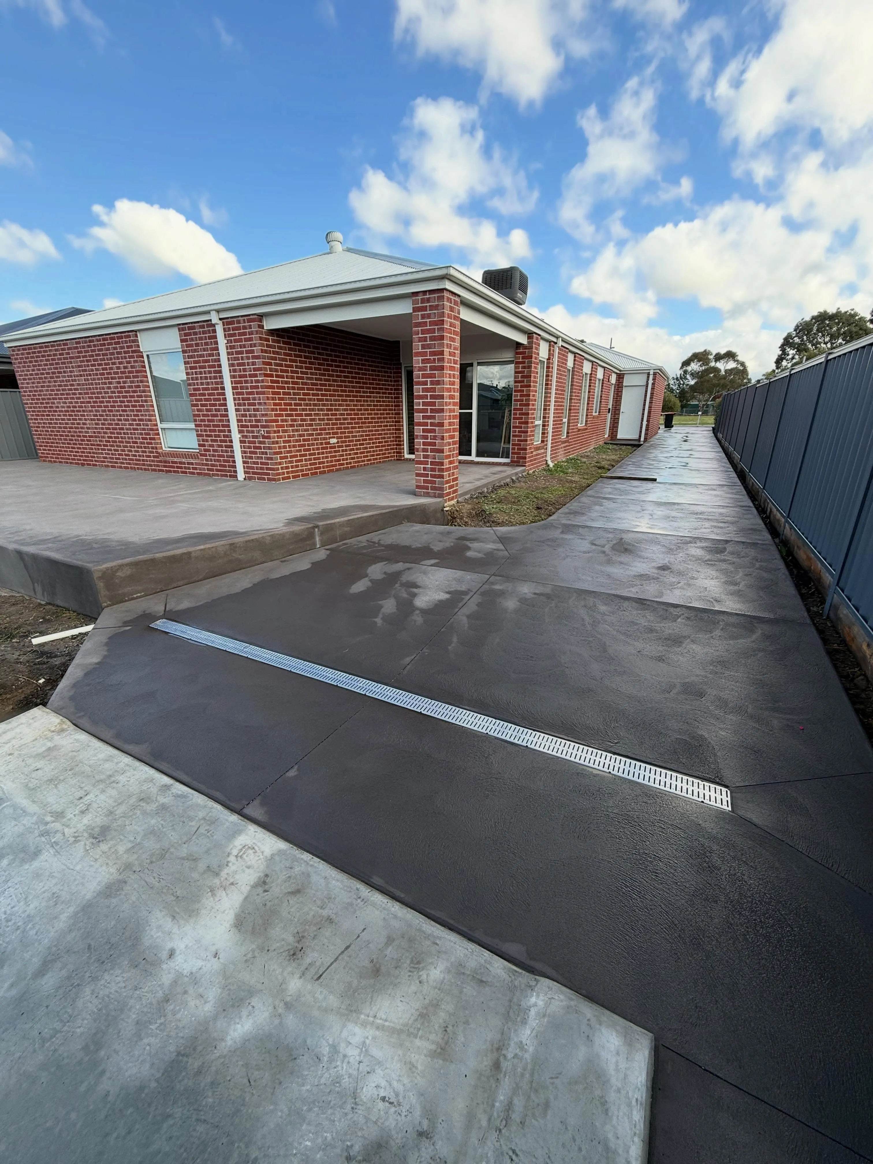 Charcoal trowelled driveway wrapping a verandah with a stainless drain channel set in