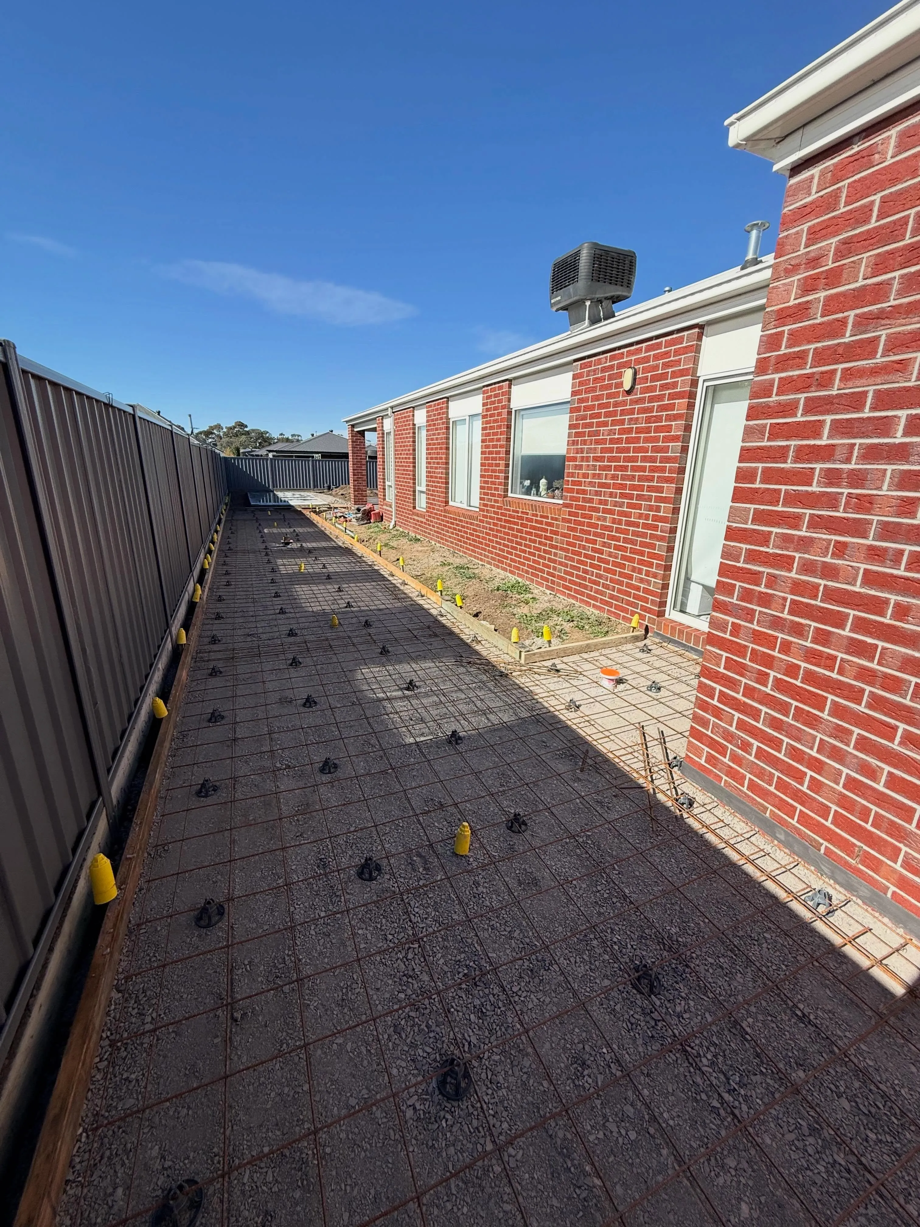 Tighter angle of the wraparound charcoal driveway showing mesh and chairs against the fence line