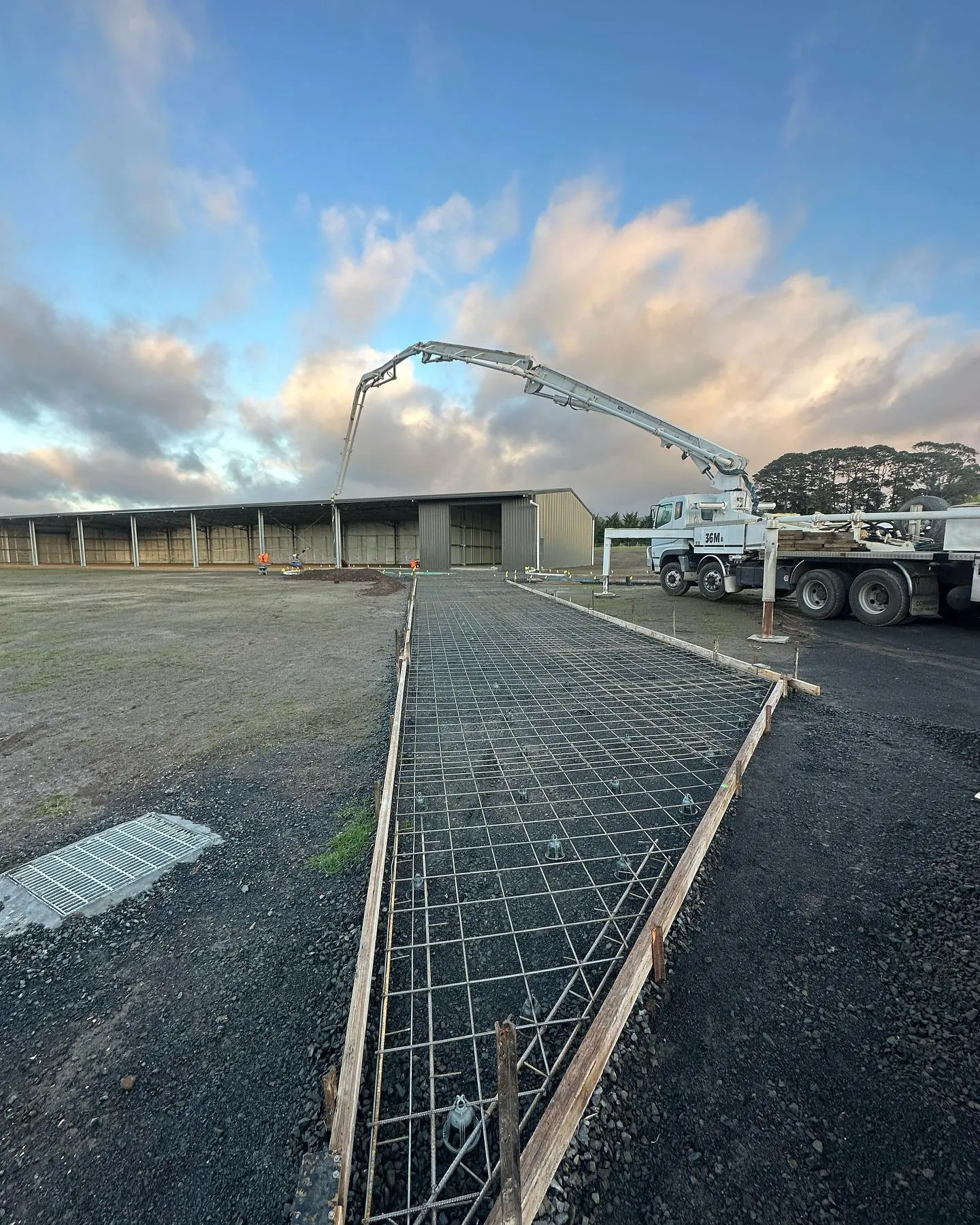 BMT branded tip truck on site with a concrete pump arm overhead and dramatic clouds