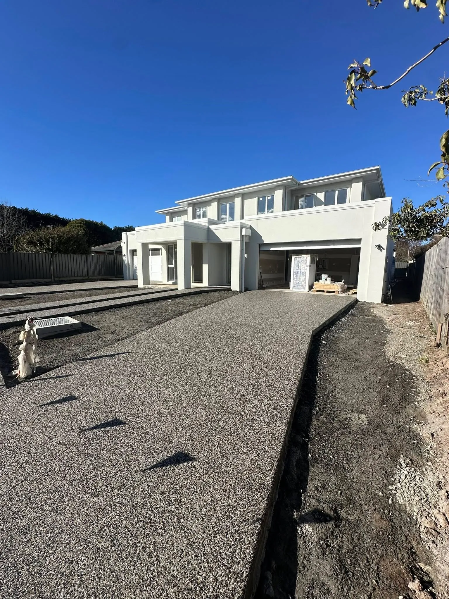 Exposed aggregate driveway leading up to a modern white two-storey home under a deep blue sky