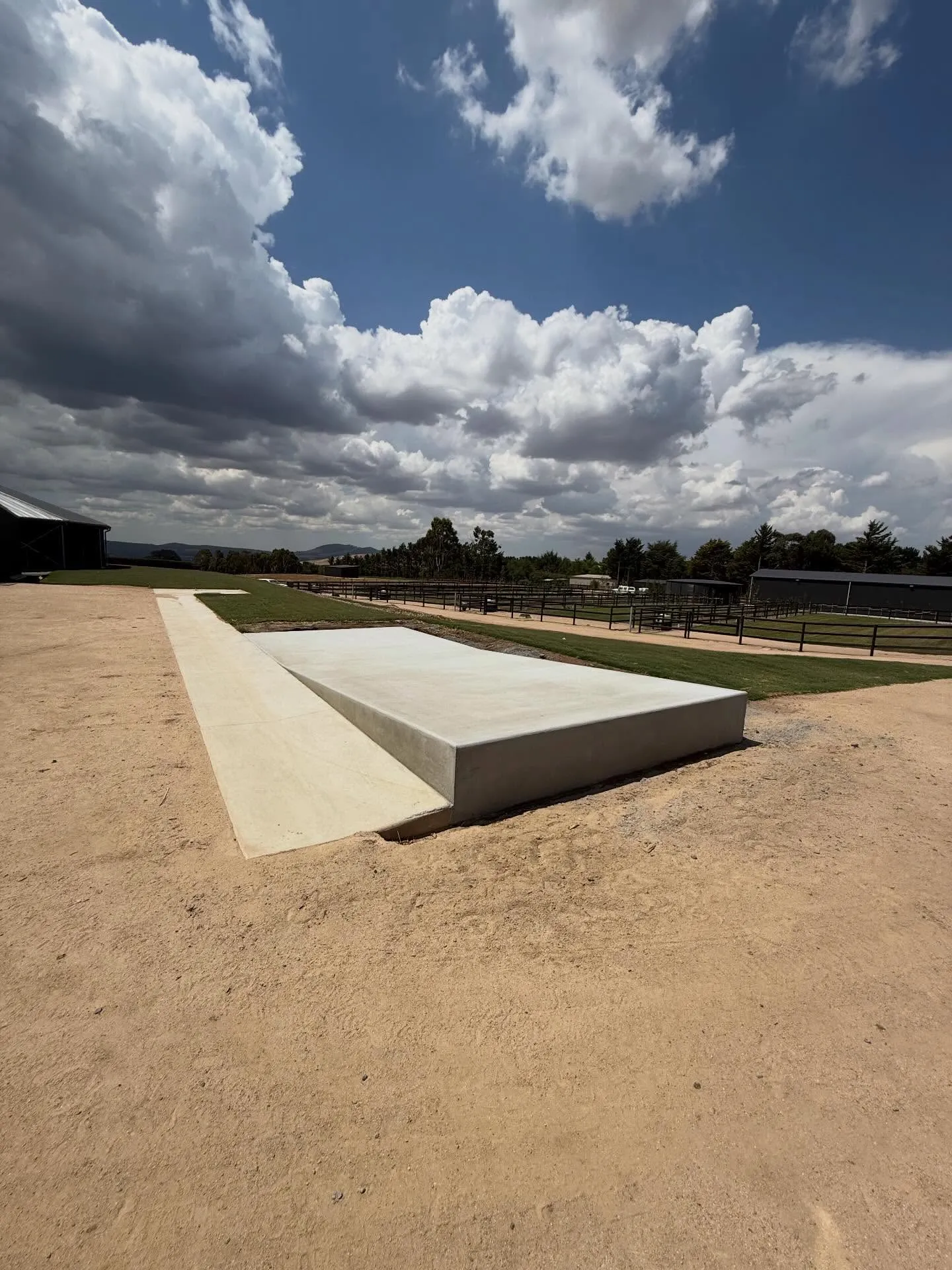 Finished concrete pad on a rural paddock with post-and-rail fencing and distant ranges