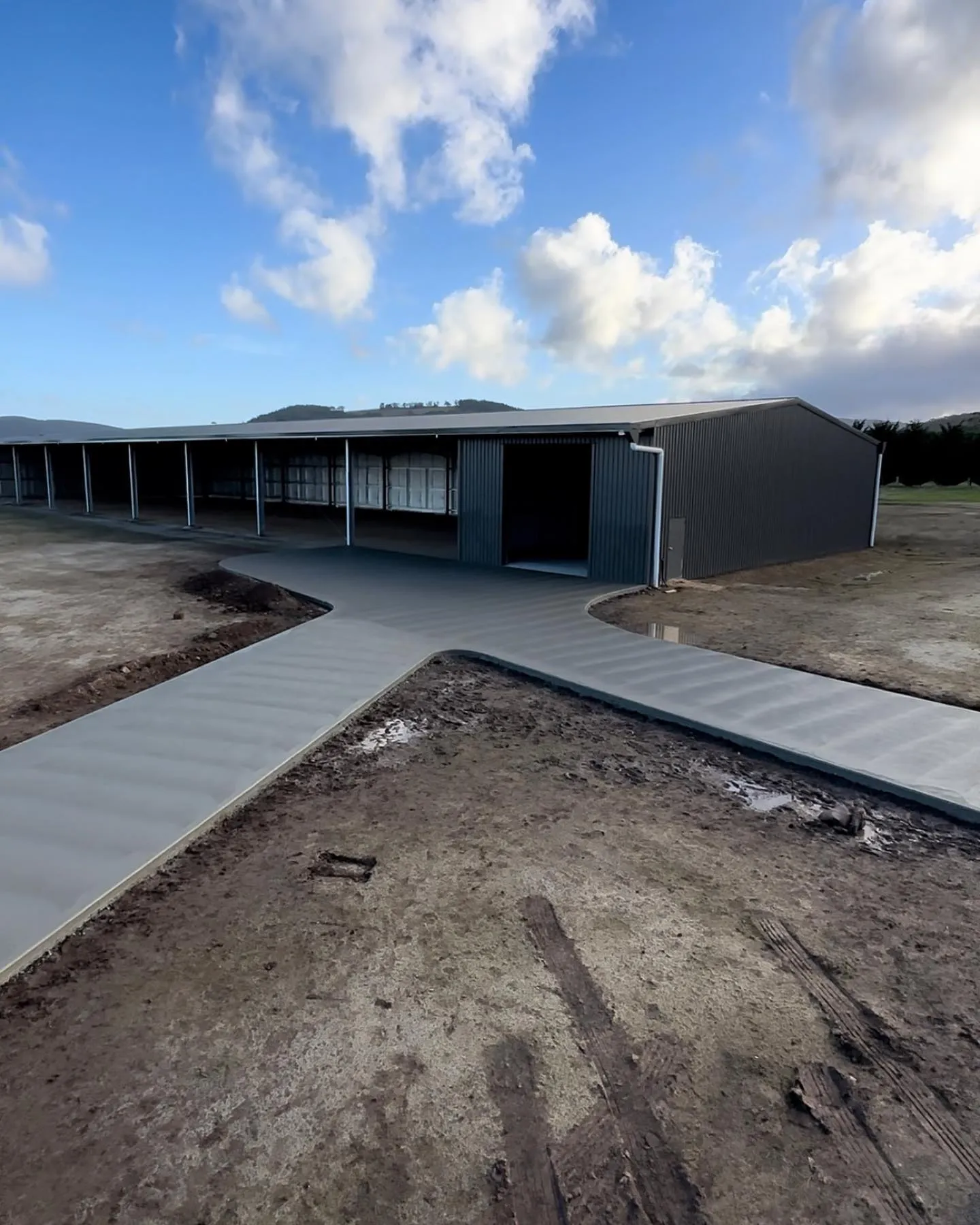 Clean concrete apron between two long open-bay sheds under a big country sky