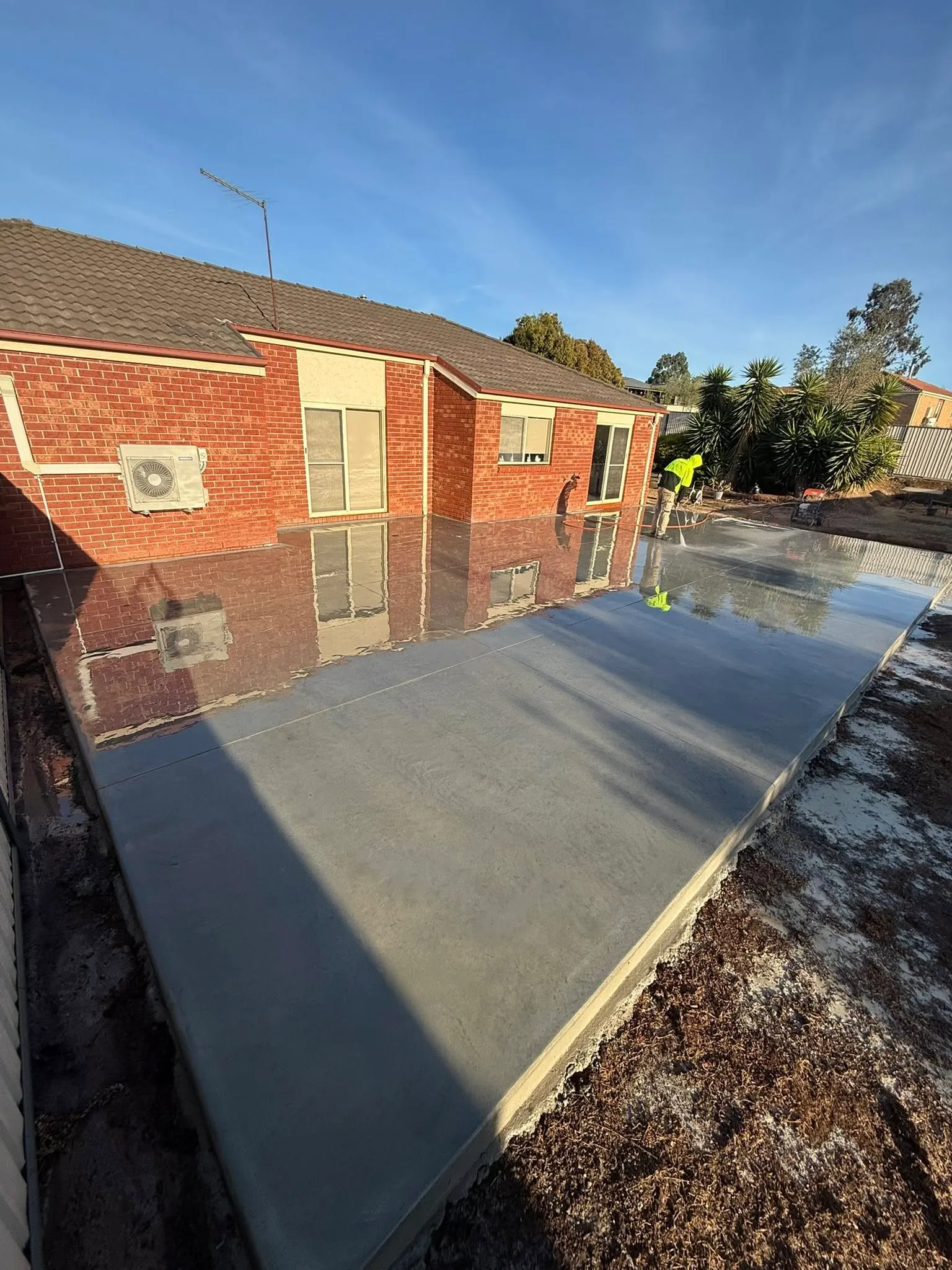 Charcoal trowelled rear patio slab behind a red-brick home with a wet finish in low sun