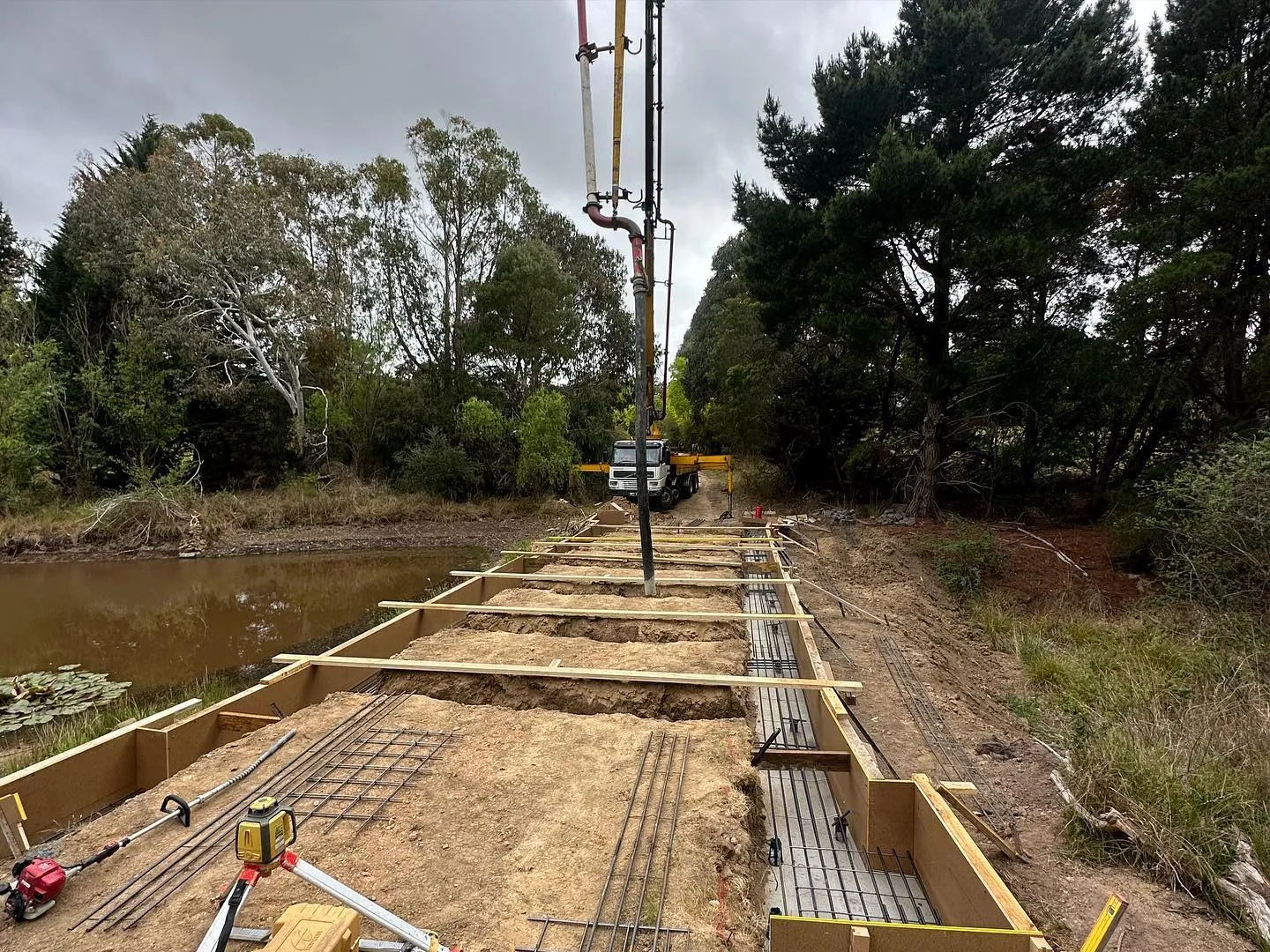 Concrete pump-truck boom feeding the dam-crossing formwork over rebar with dramatic sky behind