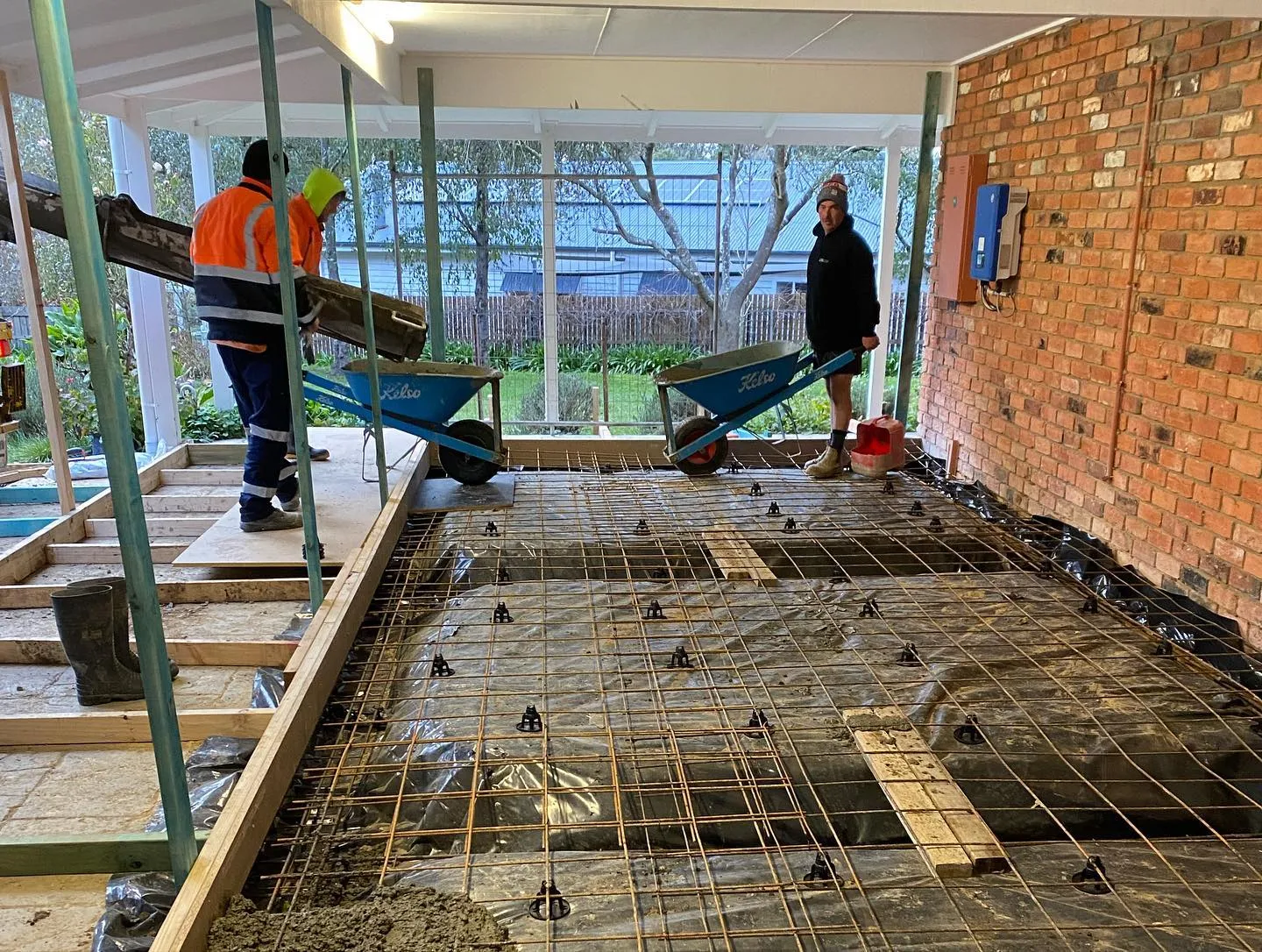 Two of the crew barrowing concrete onto interior slab formwork inside a brick courtyard