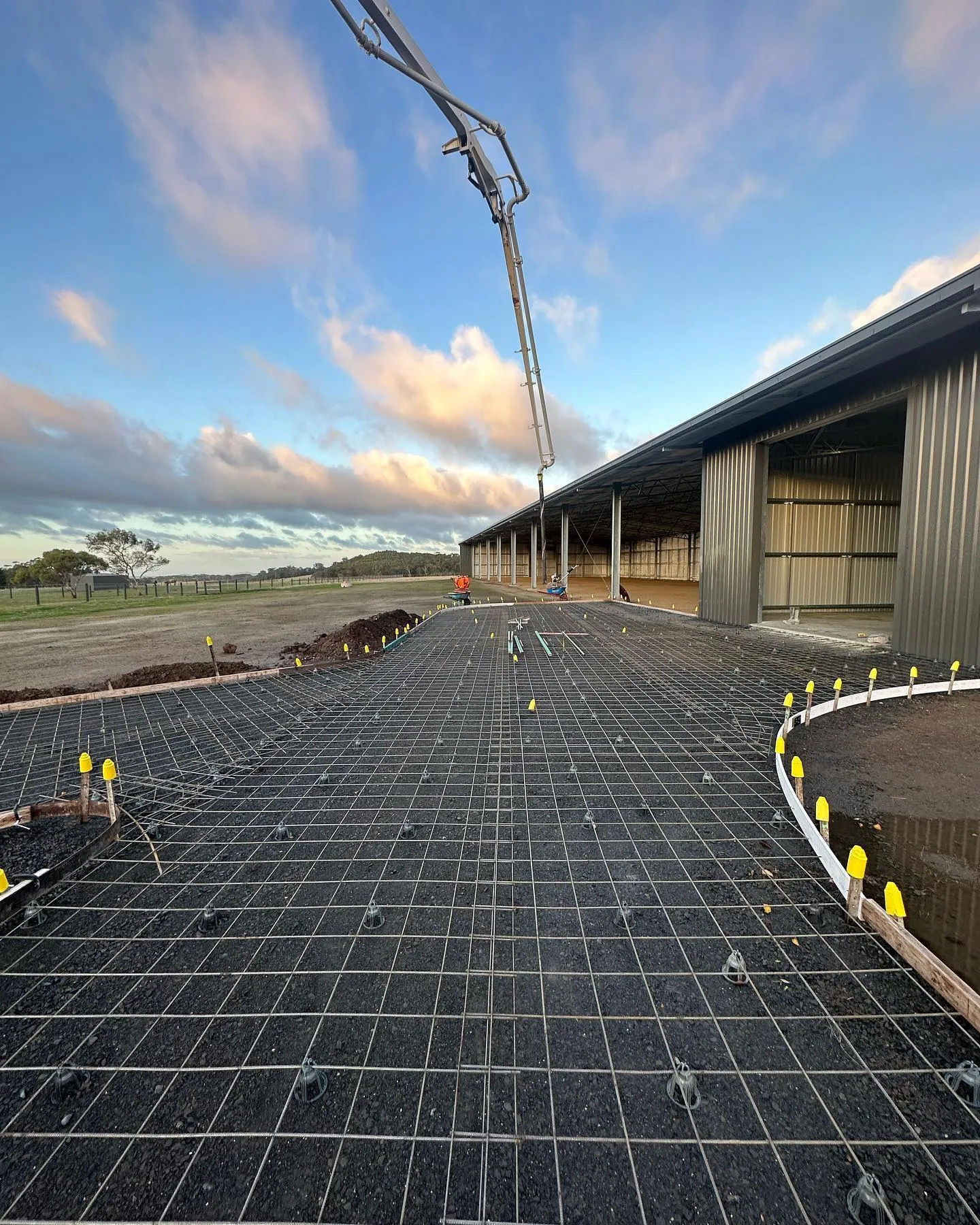 Concrete pump truck arm reaching across to the slab edge at the same shed pour, sunset sky