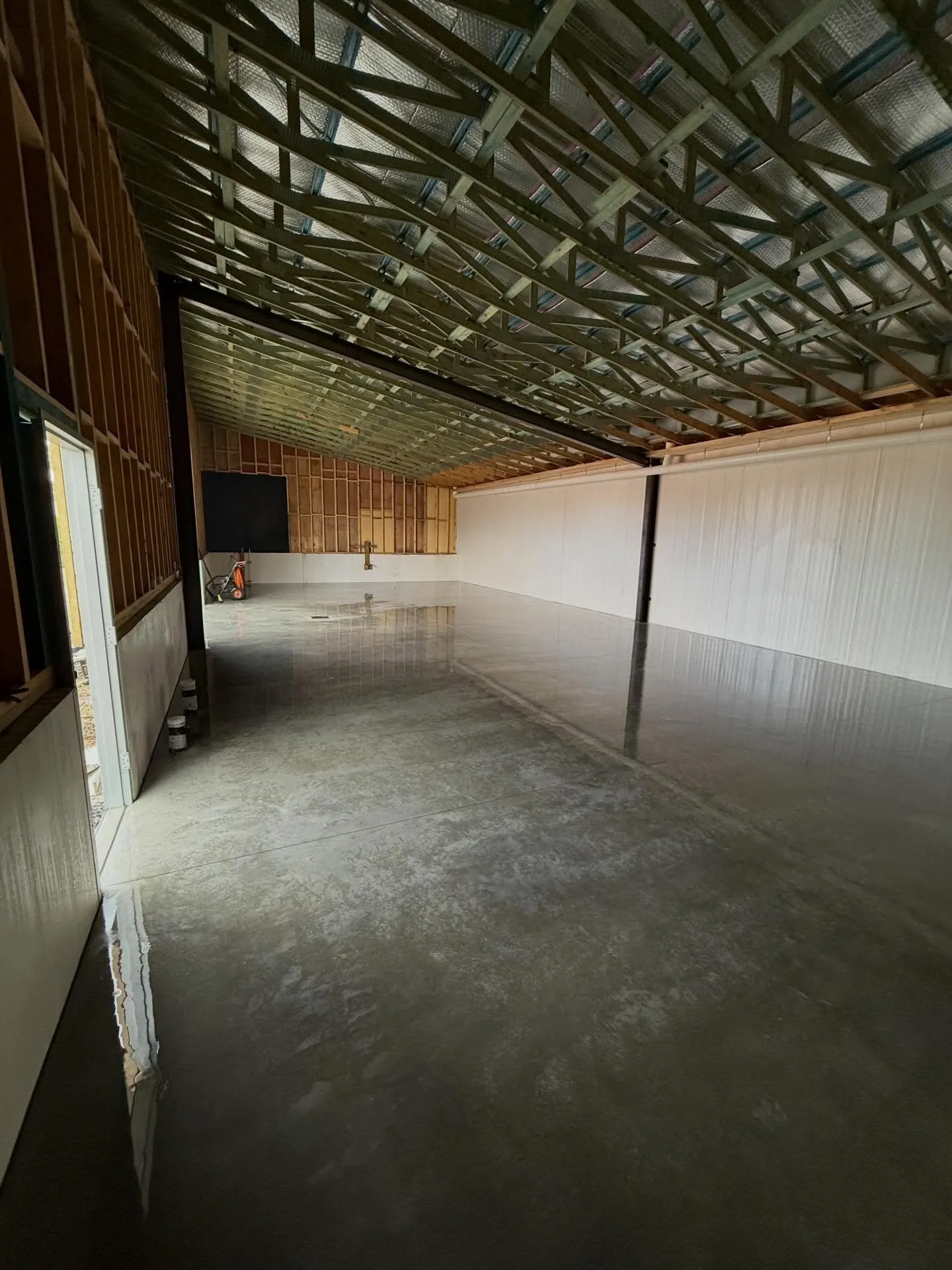 Massive wet-look high-gloss sealed warehouse floor reflecting roof trusses