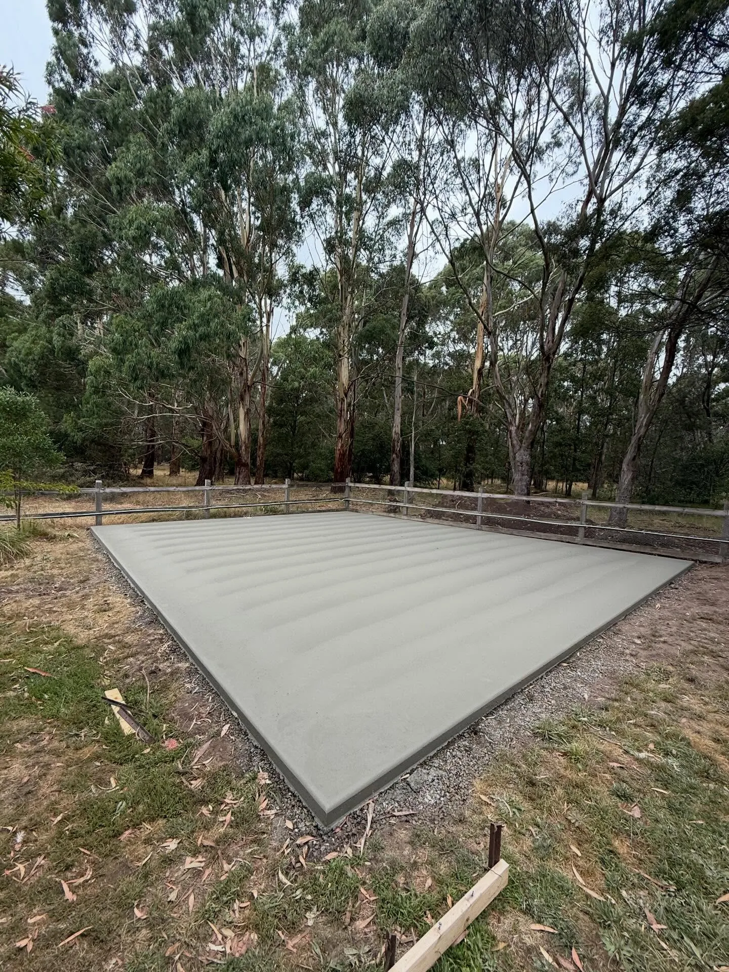 Finished square shed slab tucked into a eucalypt bush block with post-and-rail fencing