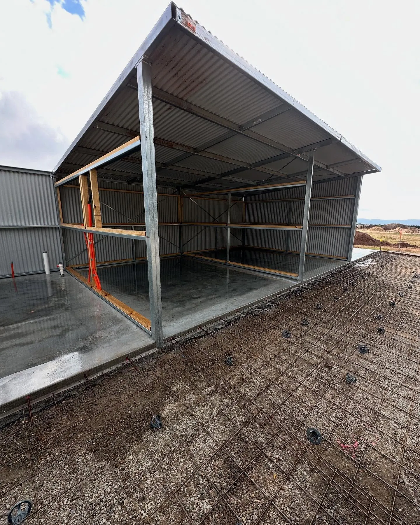 Open-fronted machinery shed with bagged reinforcement and slab prep ready for the pour, ocean horizon behind