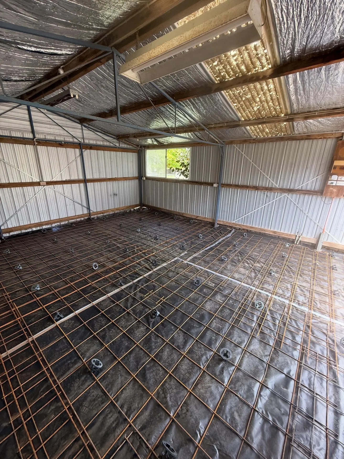 Large mesh laid on plastic under a timber and steel shed frame with foil insulation