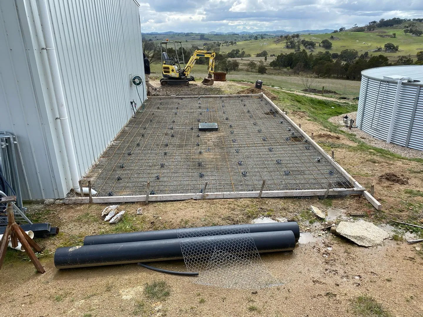 Rural shed slab prep with mesh and an excavator on a hilltop with sweeping valley views