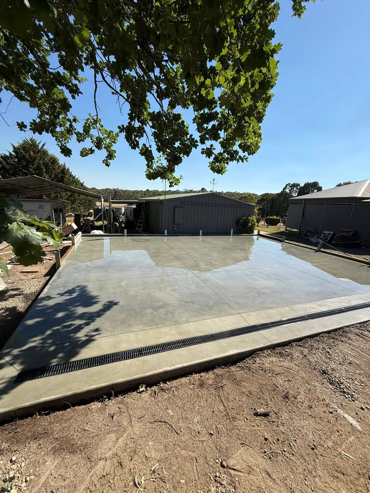 Finished large square slab in a rural yard with shedding behind and overhanging maple leaves