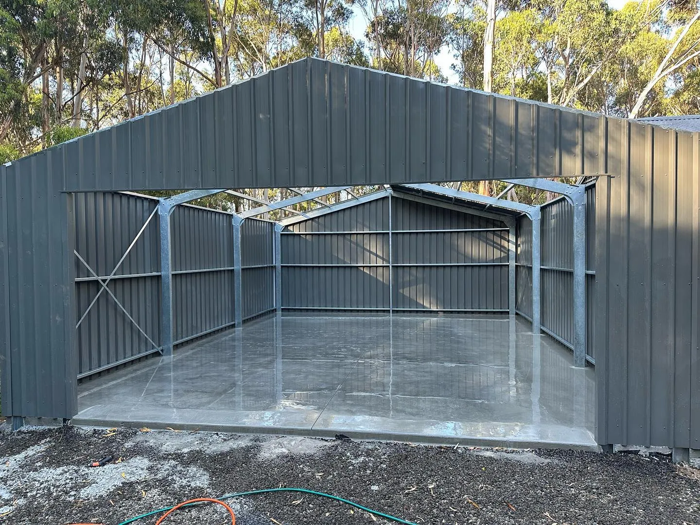 Mirror-finish trowelled shed slab inside an open-front bush garage with gum trees framing the ridge line