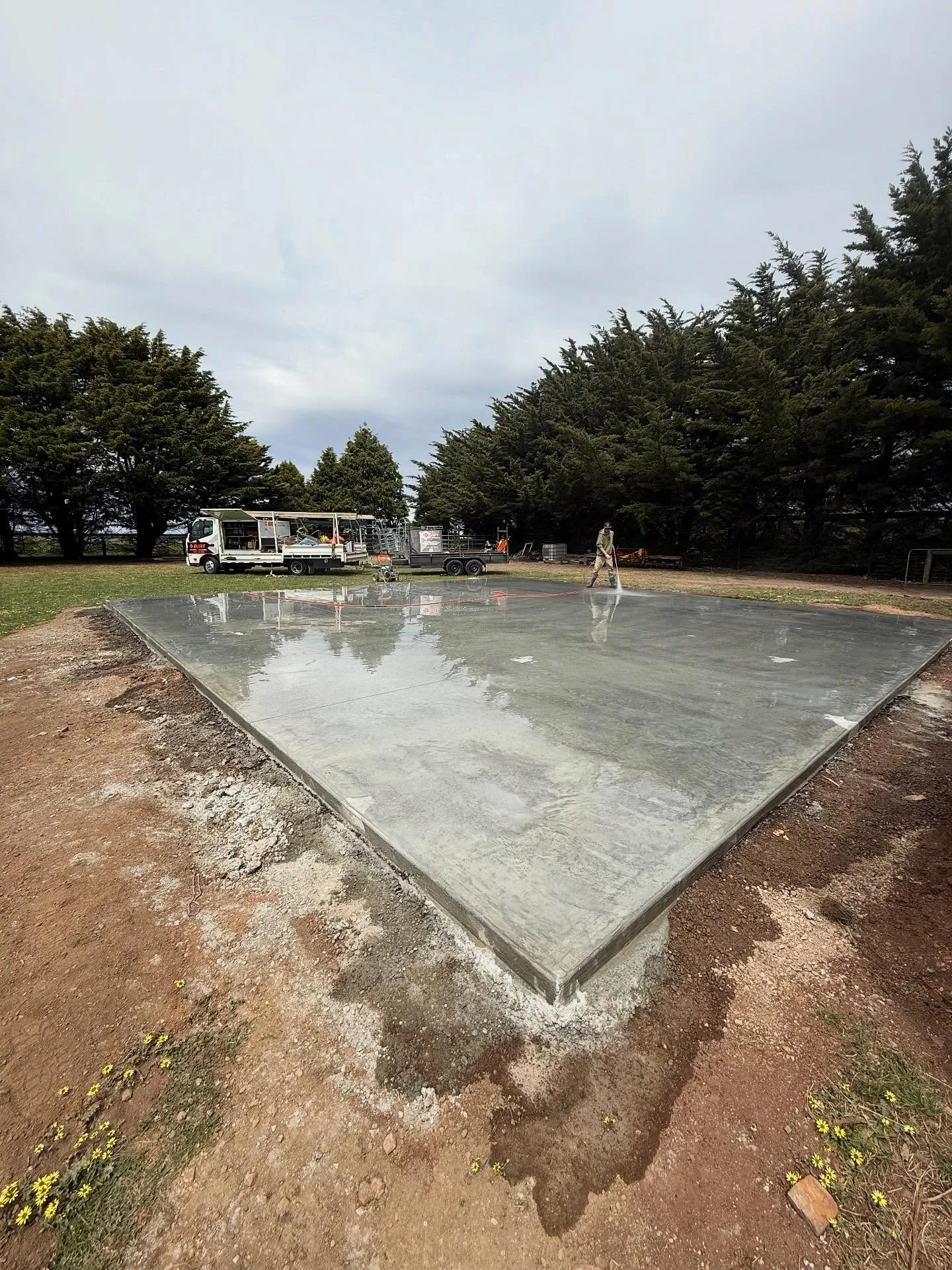 Square concrete slab pad on a rural property with a parked truck and country backdrop