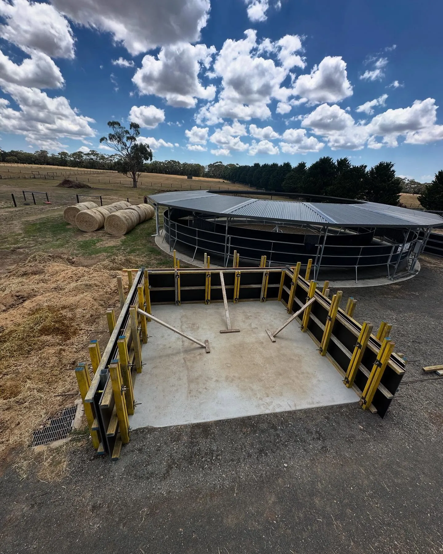 Curved steel silage pit with the finished concrete base, hay rolls and big sky across the paddock