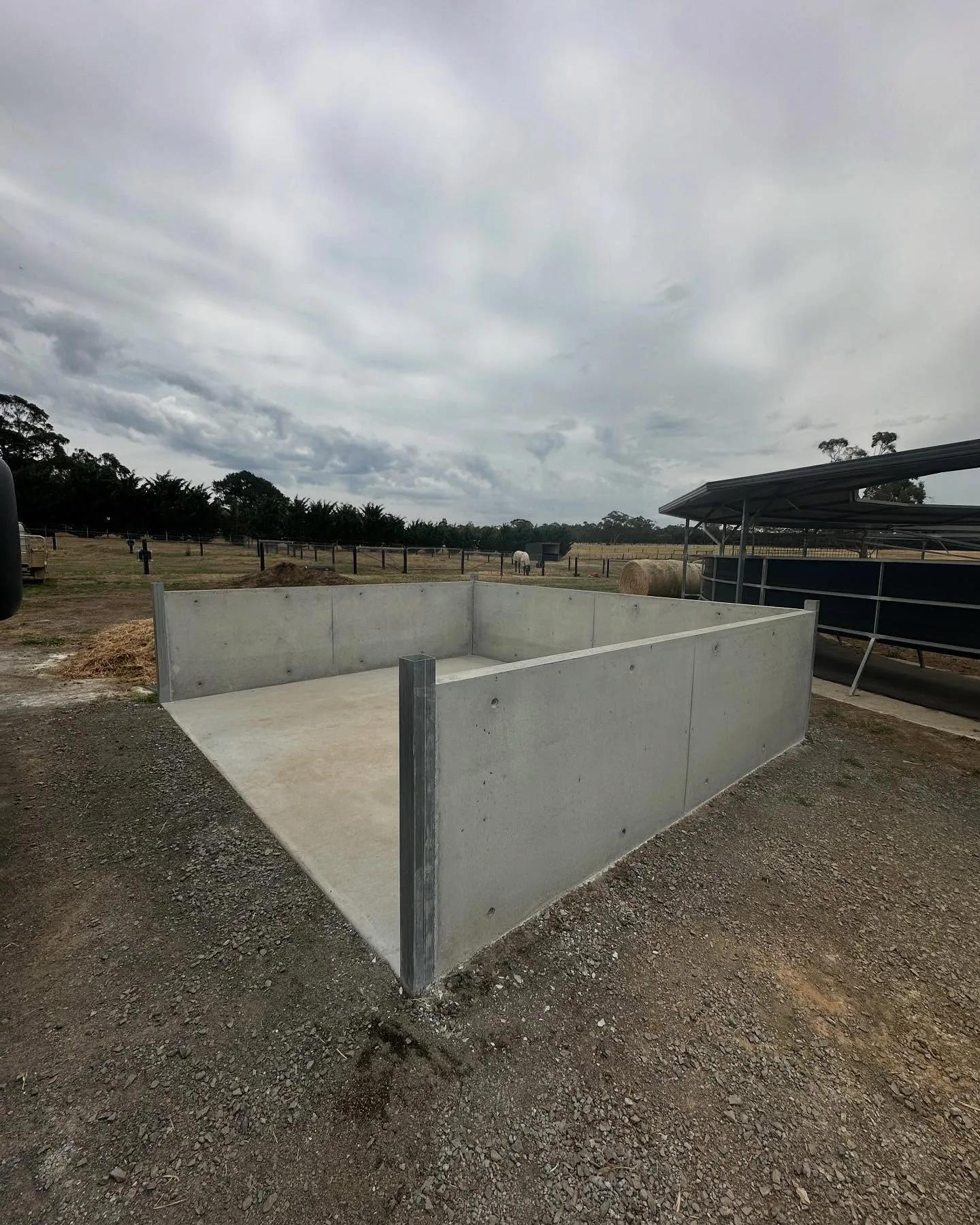 Heavy-form concrete silage bunker walls on a rural paddock with hay bales beyond