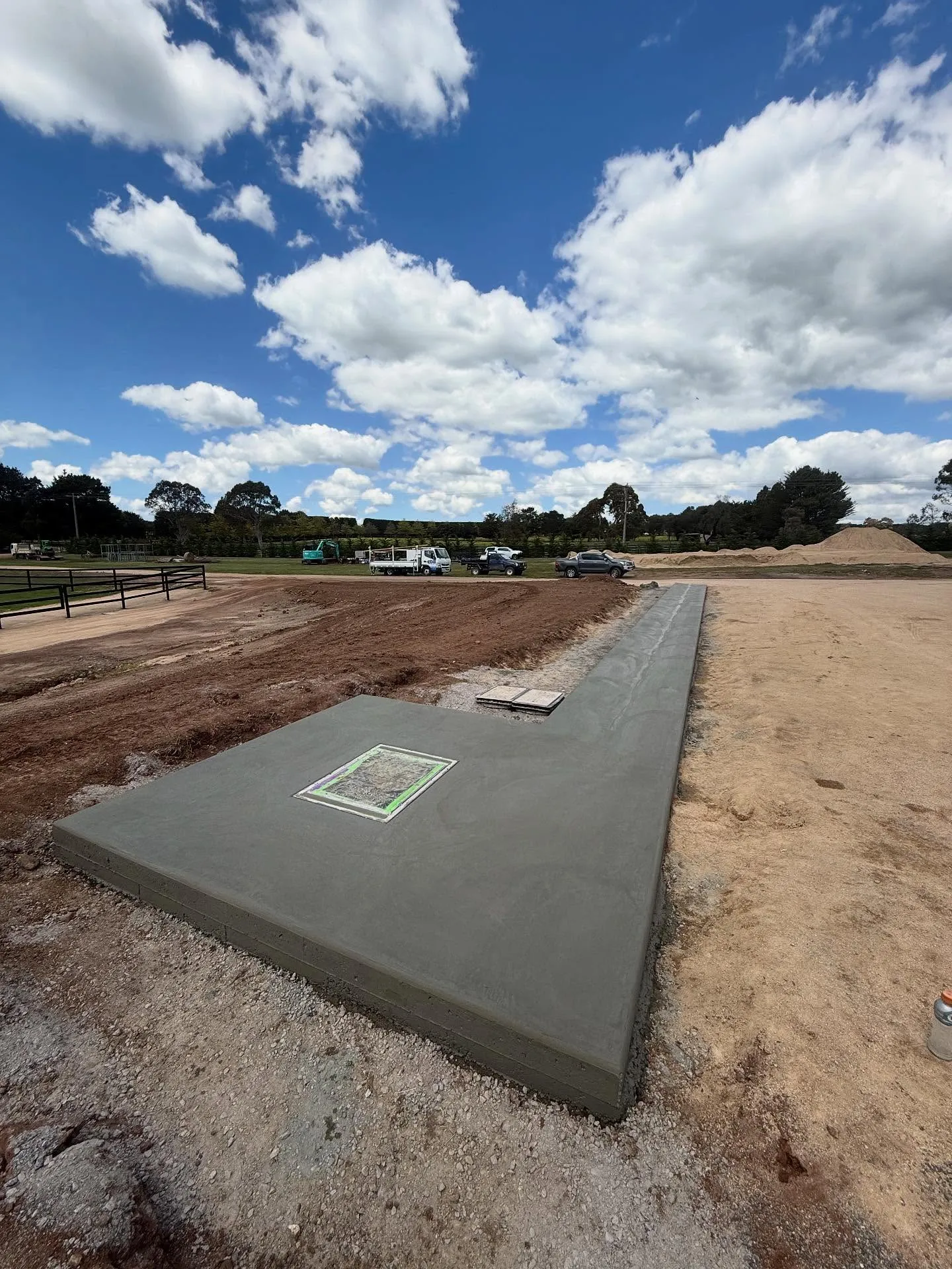 Finished concrete slab with a utility access plate set in, big white clouds overhead